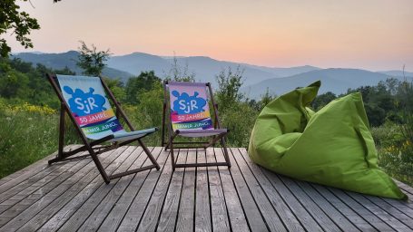 Zwei Liegestühle und ein Sitzsack auf einer Terrasse mit Blick auf die Berge bei Sonnenuntergang.