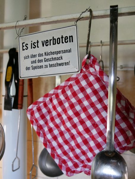 Ein rot karierter Topflappen hängt neben einem Verbotsschild in einer Küche.