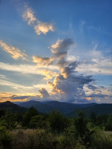 Himmel mit bunten Wolken über hügeligem Landschaftshorizont bei Sonnenuntergang.