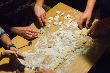 Hände formen frische Gnocchi aus Teig auf einer bemehlten Tischoberfläche.