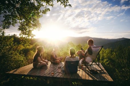 Freunde sitzen auf einer Terrasse und genießen den Sonnenuntergang über den Bergen.