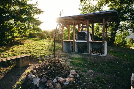 Ein schattiger Grillplatz mit einer Feuerstelle und Pizzaofen.