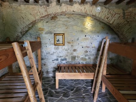 Blick auf einen Raum mit Holzbetten und einem gemauerten Bogen.