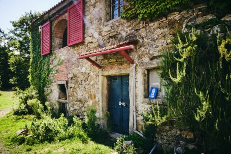 Steinernes Haus mit roten Fensterläden und grüner Pflanzenumrankung.