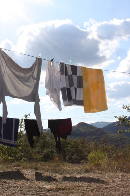 Bunte Wäsche hängt an einer Leine vor einer Landschaft mit Hügeln und Wolken.
