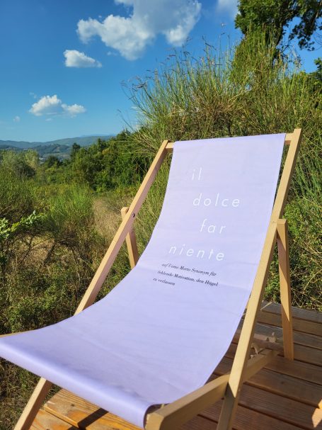 Ein Liegestuhl mit einem hellen Bezug steht in einer grünen Naturlandschaft.