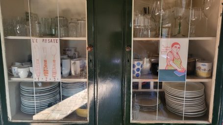 Ein Küchenschrank mit Geschirr, Gläsern und handgemalten Bildern.