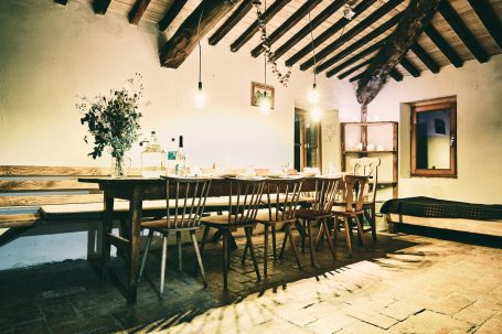 Rustikaler Essbereich mit langen Holztisch und Stühlen, warmes Licht, sichtbare Holzbalken.