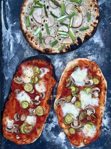 Drei Pizzas auf einem Blech: eine mit Zwiebeln und Paprika, zwei mit Tomatensauce und Gemüse.